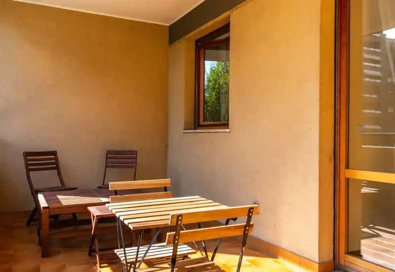 Balcone soleggiato arredato con tavolo e sedie in legno, pavimento piastrellato e luce naturale — ideale per relax o pasti all'aperto.