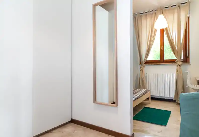 Coin de chambre avec un lit simple près d'une fenêtre habillée de rideaux légers ; propre, lumineux et sobrement meublé — idéal pour un invité ou un étudiant.