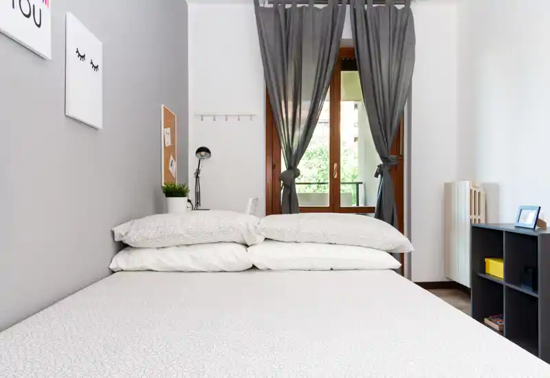 Bright, modern bedroom with a neatly made double bed facing a window. Neutral tones, simple décor and natural light create a calm, welcoming space.
