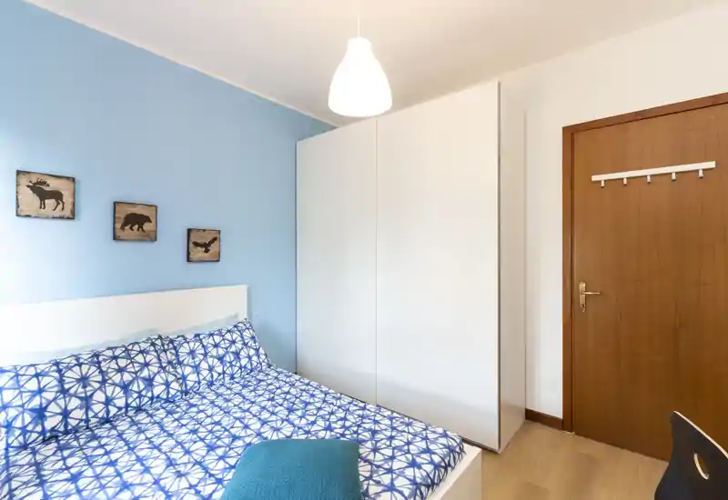 Dormitorio compacto y luminoso con edredón azul estampado, armario blanco y suelo de madera clara — bien presentado para alquileres.