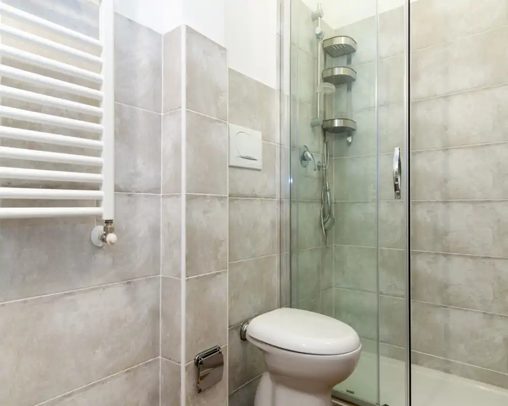 Baño moderno y compacto con paredes alicatadas, mampara de ducha de cristal e inodoro; luminoso, limpio y bien cuidado.