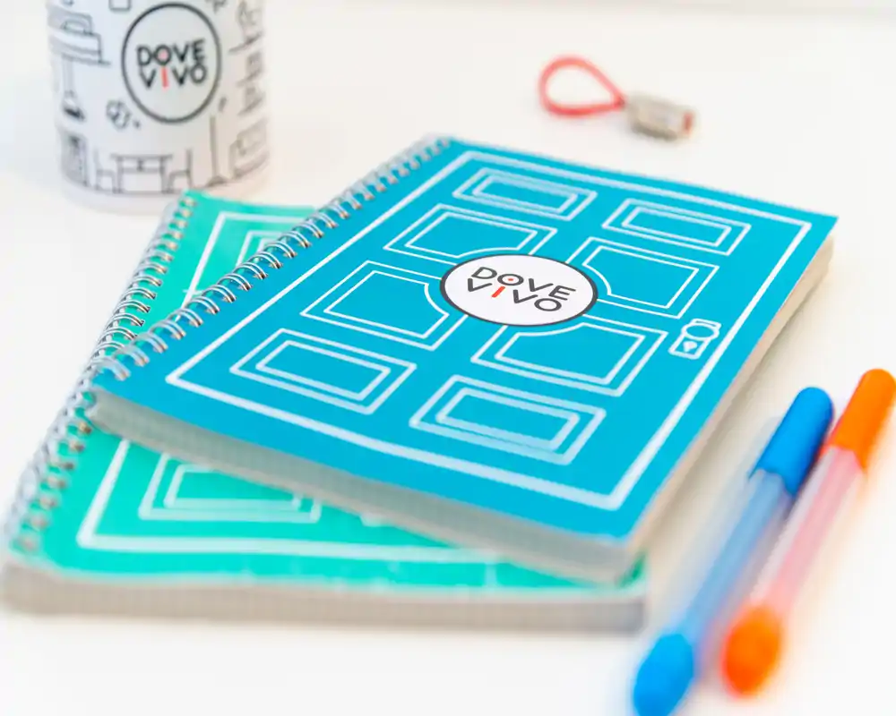 Gros plan de deux carnets à spirale et de quelques stylos colorés sur une surface blanche propre — photo d'articles de papeterie/produit, ne montrant aucune pièce identifiable.