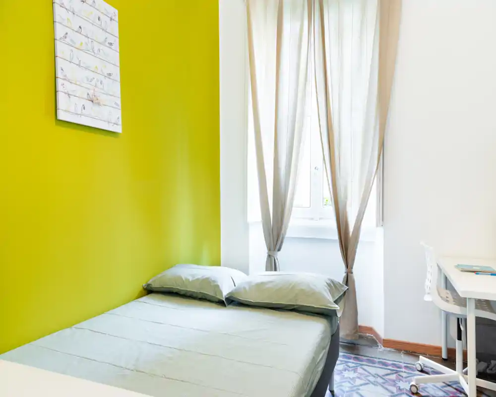 Chambre lumineuse et moderne avec un lit double contre un mur vert vif, coussins moelleux et une fenêtre voilée laissant entrer une belle lumière naturelle.