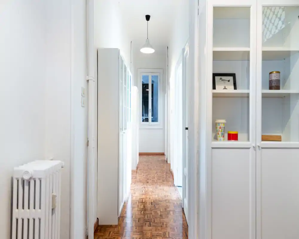 Corridoio/ingresso luminoso e pulito con armadi bianchi a muro, pavimento in parquet e una finestra sul fondo che dona luce naturale — perfetto come ingresso accogliente.