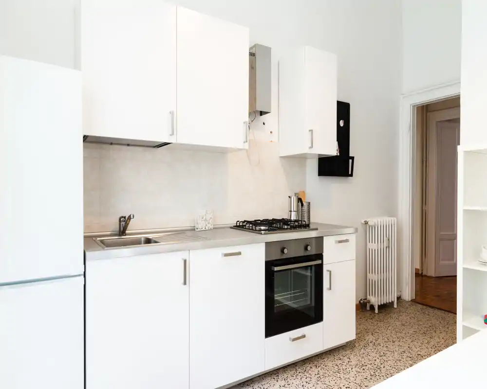 Cucina moderna e luminosa con mobili bianchi, lavello in acciaio, forno incassato e piano cottura a gas; stile pulito e minimale adatto a un annuncio immobiliare.