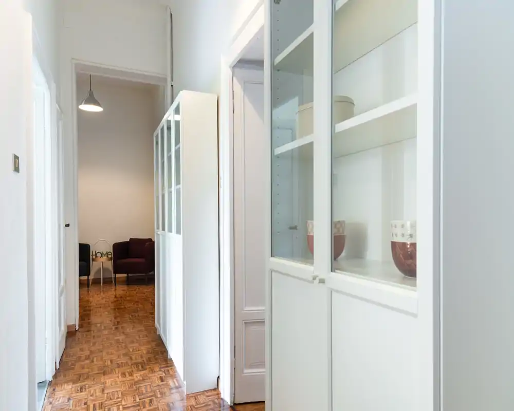 Ingresso/corridoio luminoso e ordinato con pavimento in parquet e armadi bianchi a muro, che conduce a un piccolo angolo conversazione. Buona illuminazione e presentazione curata ideale per un annuncio.