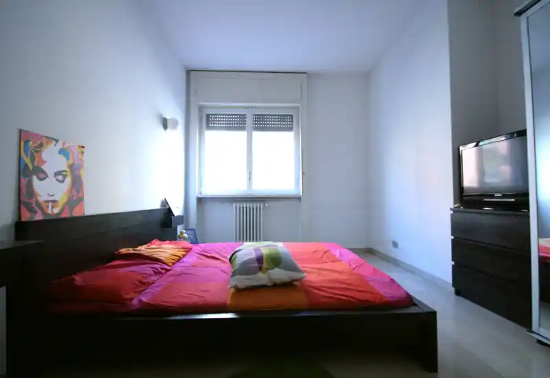 Dormitorio moderno y luminoso con cama baja de madera oscura y ropa de cama colorida frente a una gran ventana que aporta luz natural.