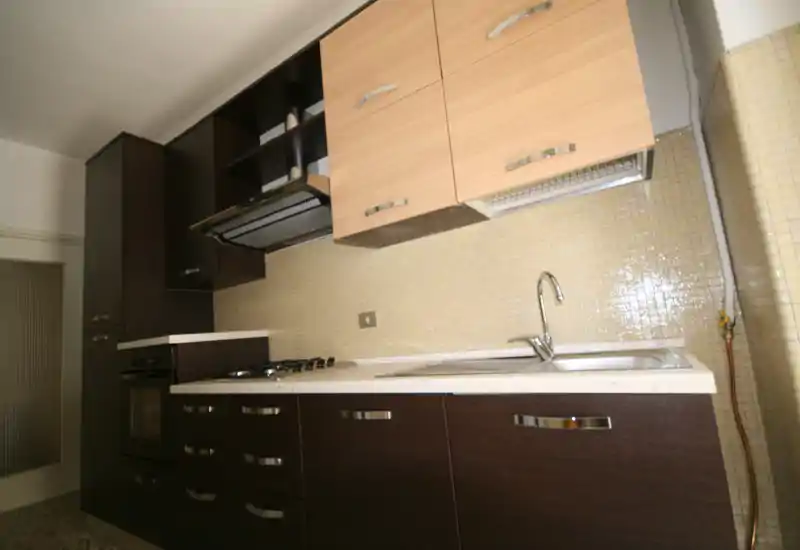 Cocina contemporánea con mobiliario inferior oscuro, armarios superiores claros y salpicadero de azulejos. Incluye horno empotrado, placa de gas y fregadero de acero; distribución limpia para anuncios.