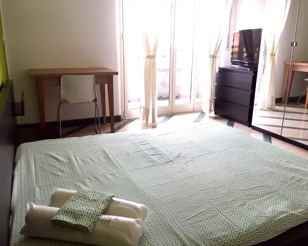 Bright, neatly made bedroom with a large low bed, folded towels and direct natural light from French doors — comfortable and well-styled for a rental listing.