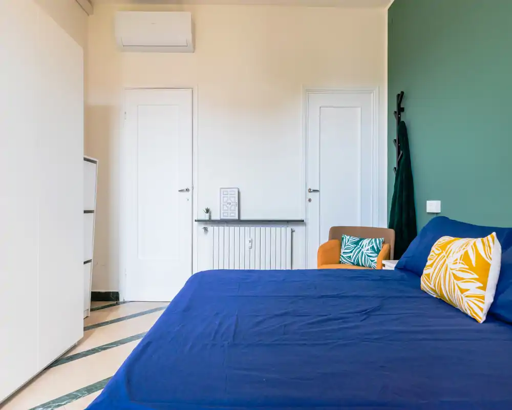 Bright, tidy bedroom with a large bed dressed in deep blue linens, decorative pillows and a cozy armchair beside it — modern, welcoming space ideal for rental photos.