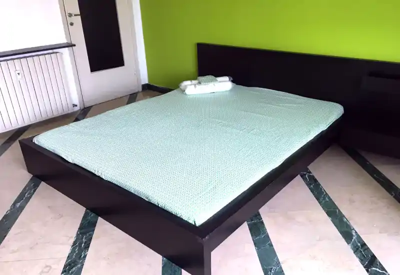 Modern bedroom with a large dark-framed bed, mint bedding and neatly folded towels; bright, minimal and well-presented space ideal for rental photos.