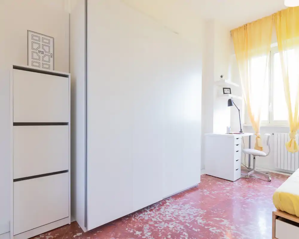 Dormitorio luminoso y minimalista con armario blanco empotrado, escritorio junto a la ventana y cortinas amarillas que aportan calidez.