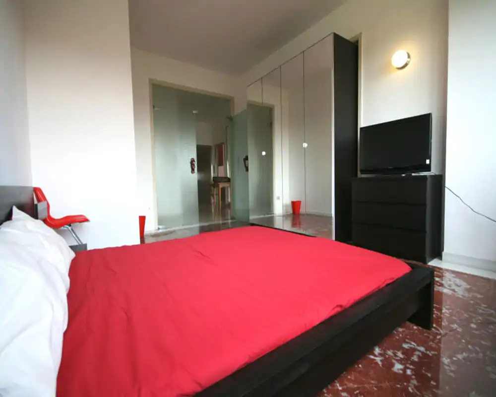 Dormitorio moderno y luminoso con cama baja y edredón rojo intenso, mobiliario oscuro y armario con espejo que amplía el espacio.
