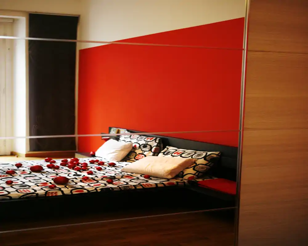 Camera da letto elegante con biancheria a motivo, cuscini decorativi e una parete rossa d'accento. La luce naturale dalla finestra crea un'atmosfera calda e accogliente.