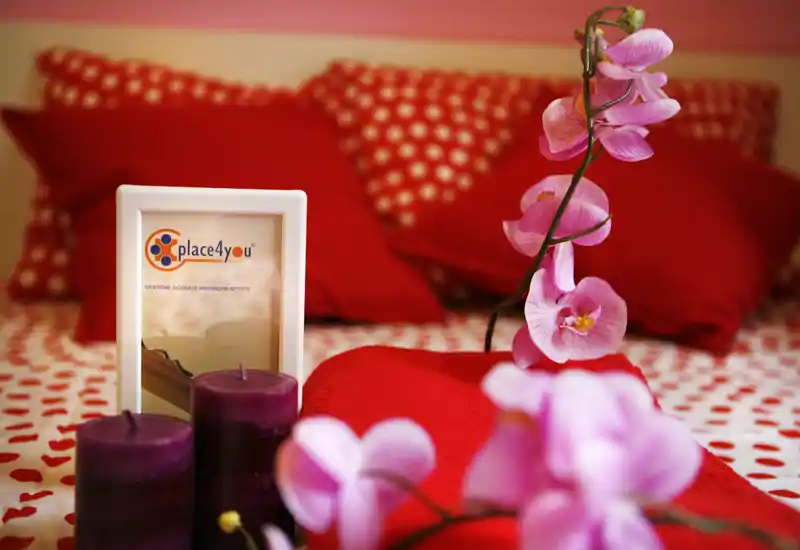 Cozy bedroom scene with red pillows and patterned bedding, accented by purple candles and pink orchid blooms; warm, well-styled shot ideal for a rental listing.