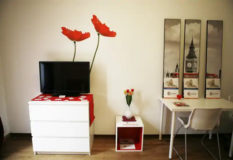 Área de estar luminosa y cuidada con televisor sobre sinfonier blanco, arte mural y un pequeño escritorio — moderna, acogedora y bien iluminada.