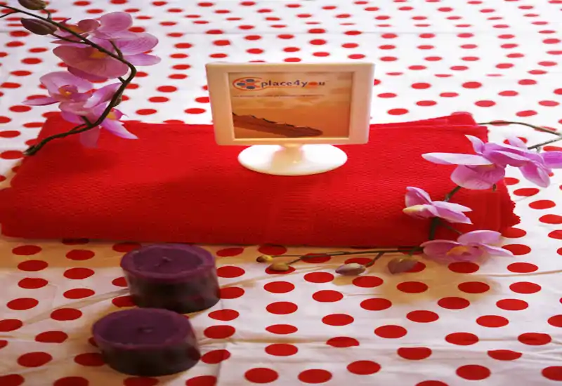 Primer plano de un arreglo decorativo: toalla roja doblada, orquídeas decorativas y dos velas moradas sobre una superficie de lunares rojos — perfecto para destacar detalles de baño o bienestar.