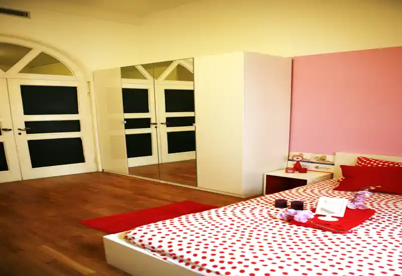 Bright, cozy bedroom with a white platform bed dressed in red-and-white polka-dot linens, bedside table and a mirrored wardrobe that adds depth.