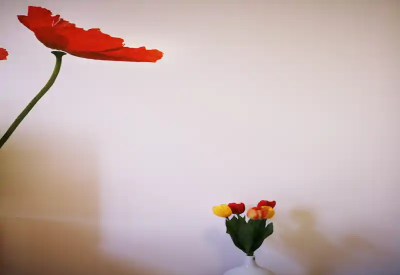 Primer plano de una pared decorativa con un gran motivo floral rojo y un pequeño jarrón con tulipanes sobre un fondo claro; imagen artística, no una vista de la habitación.