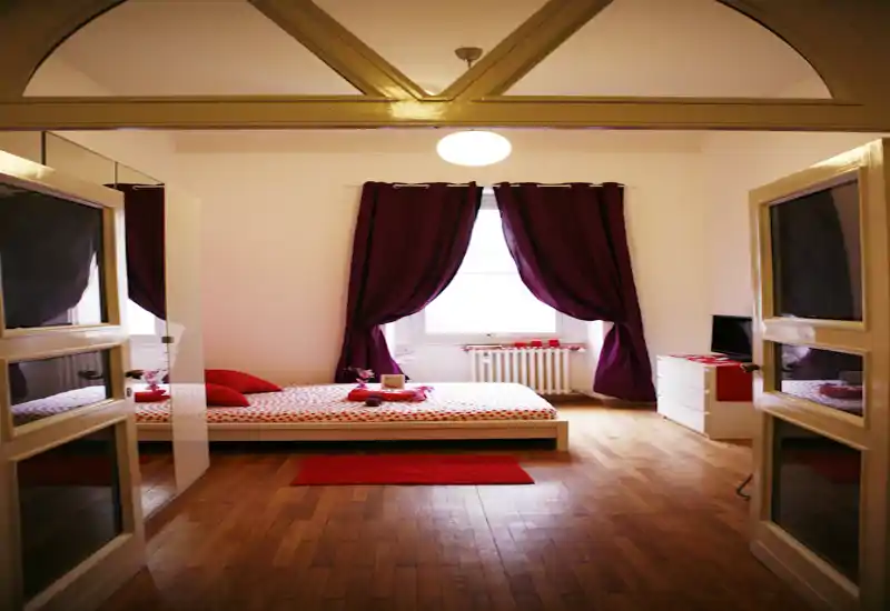 Spacious, styled bedroom with a low platform bed set against a window framed by deep purple curtains, wooden floors and warm, coordinated accents.
