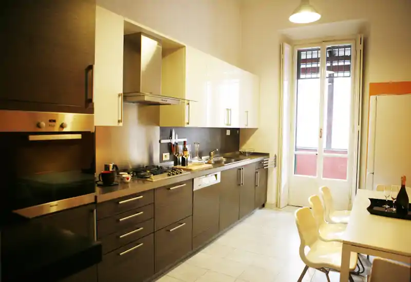 Cocina moderna y luminosa con larga encimera, horno empotrado, placa de gas y zona de comedor junto a una puerta acristalada que aporta luz natural.