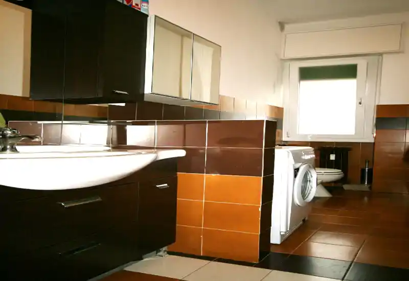 Salle de bain compacte avec lavabo, armoire-miroir, machine à laver et toilettes ; carrelage marron et orange apportant une ambiance chaleureuse et rétro.