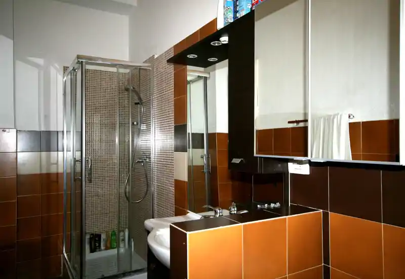 Baño moderno y limpio con ducha con mampara de cristal, lavabo con espejo-armario y azulejos marrones cálidos.