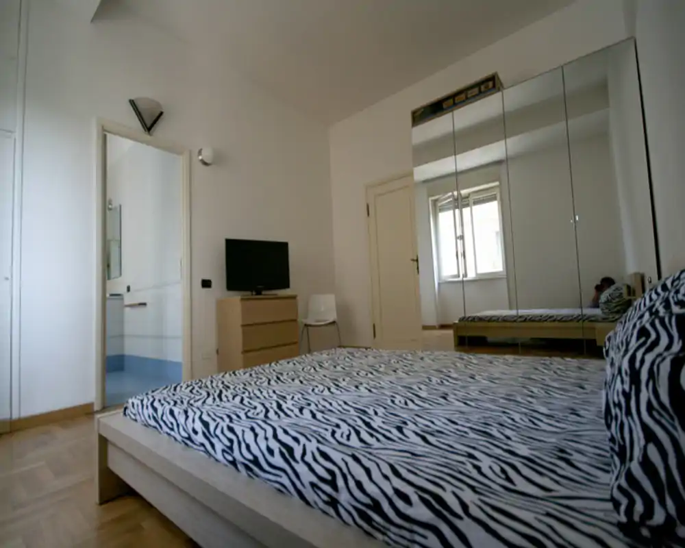 Dormitorio moderno y luminoso con cama baja de estampado cebra, armario con espejos que amplía el espacio y cómoda con TV — aireado y minimalista.