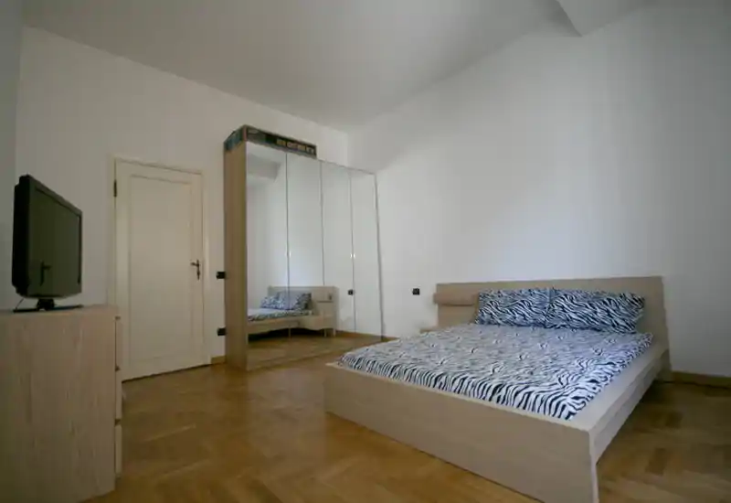Camera da letto luminosa e minimale con letto matrimoniale basso in legno e biancheria a fantasia zebra, armadio con ante a specchio e pavimento in parquet. Ambiente pulito e ordinato, adatto per annunci di affitto.