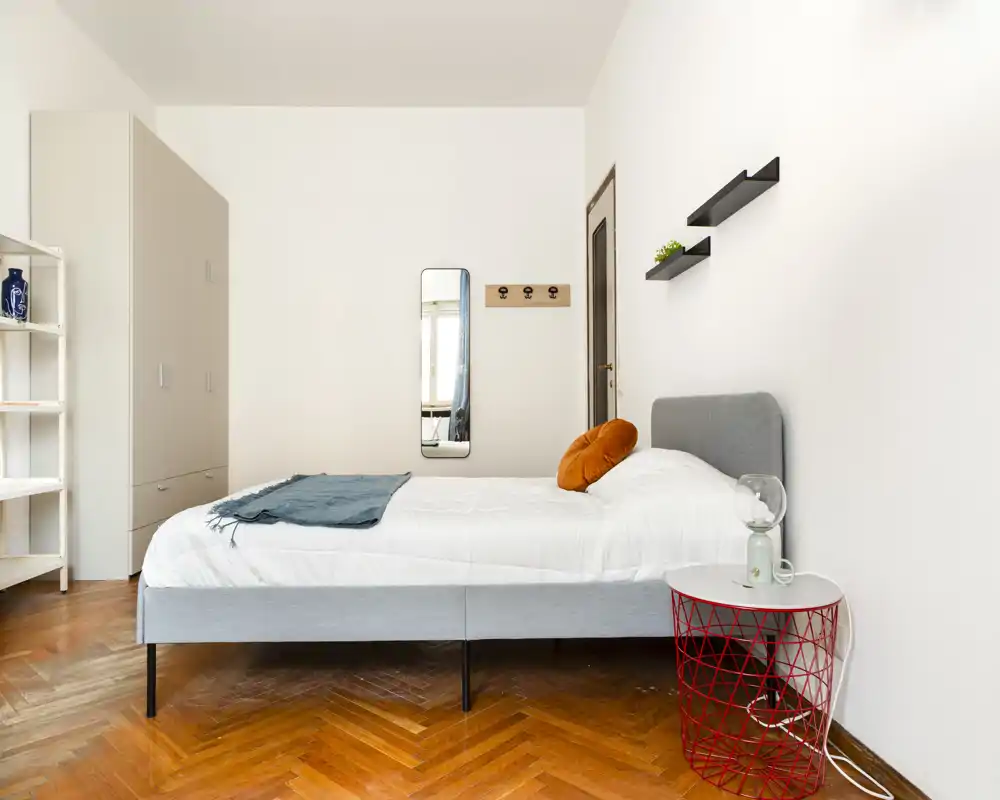Camera da letto luminosa e minimale con letto intero, pavimento in parquet caldo e arredi moderni semplici. Lo spazio risulta arioso e accogliente grazie alla luce naturale e ai dettagli curati.