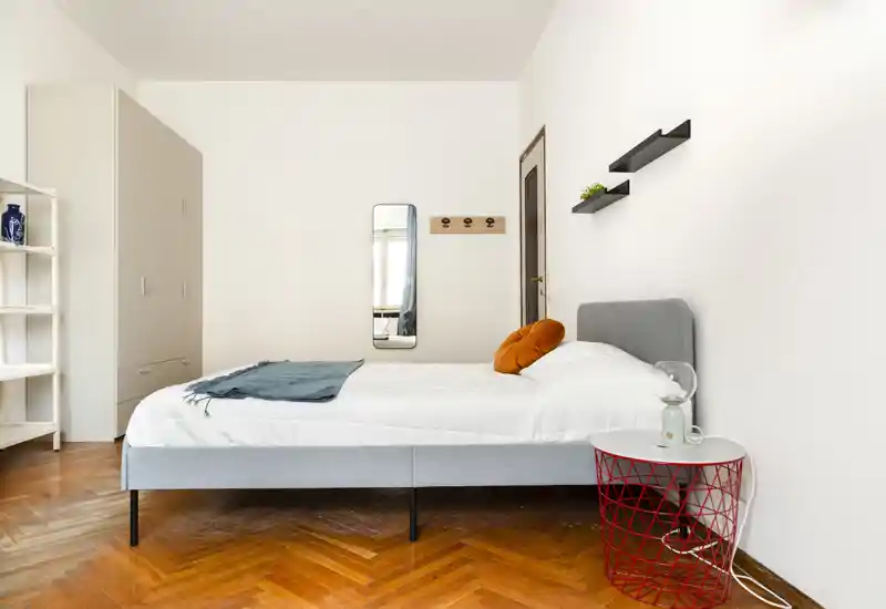Camera da letto luminosa e minimale con letto intero, pavimento in parquet caldo e arredi moderni semplici. Lo spazio risulta arioso e accogliente grazie alla luce naturale e ai dettagli curati.