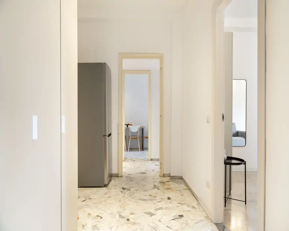 Ingresso luminoso e minimal con pavimento effetto marmo, pareti bianche pulite e porta che conduce alle stanze adiacenti; spazio di collegamento moderno e accogliente.