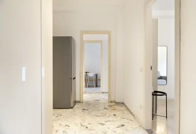 Entrada luminosa y minimalista con suelo efecto mármol, paredes blancas limpias y puerta que da acceso a habitaciones contiguas; espacio de circulación moderno y acogedor.