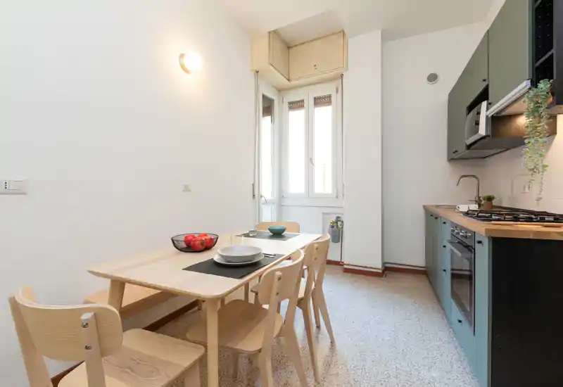 Coin repas moderne et lumineux intégré à une cuisine compacte. Une table en bois avec quatre chaises est placée près d'une grande fenêtre apportant une belle lumière naturelle.