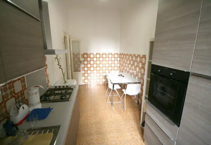 Cuisine lumineuse et compacte avec meubles effet bois, four encastré et plaques à gaz, ainsi qu'une petite table contre un mur carrelé rétro.