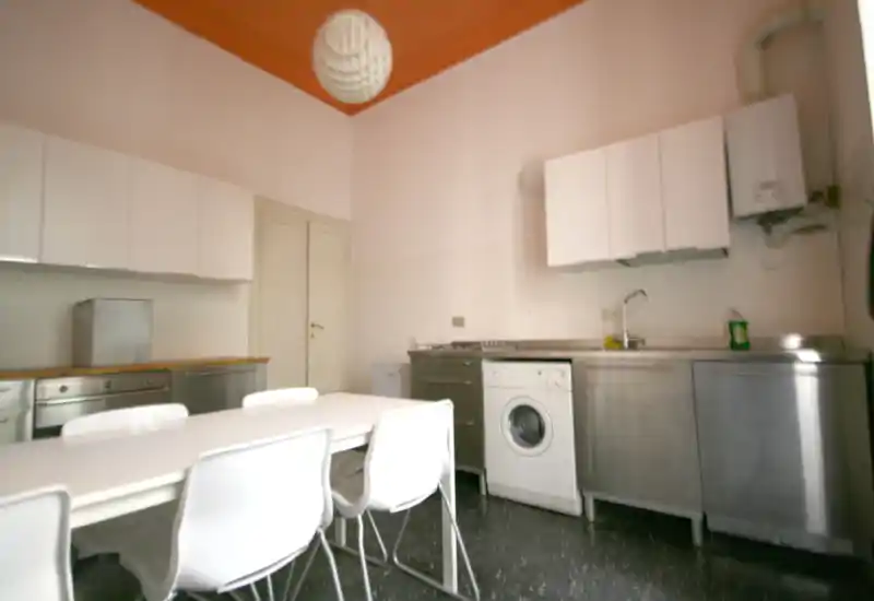 Functional kitchen with stainless-steel countertops, built-in appliances and a simple dining table; bright ceiling detail adds character.