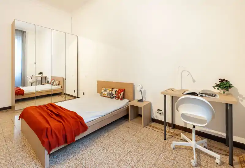 Camera da letto luminosa e minimal con letto singolo in legno, armadio con ante a specchio e una piccola scrivania. Linee pulite e accenti caldi (coperta e cuscini) rendono l'ambiente accogliente e funzionale per una persona.