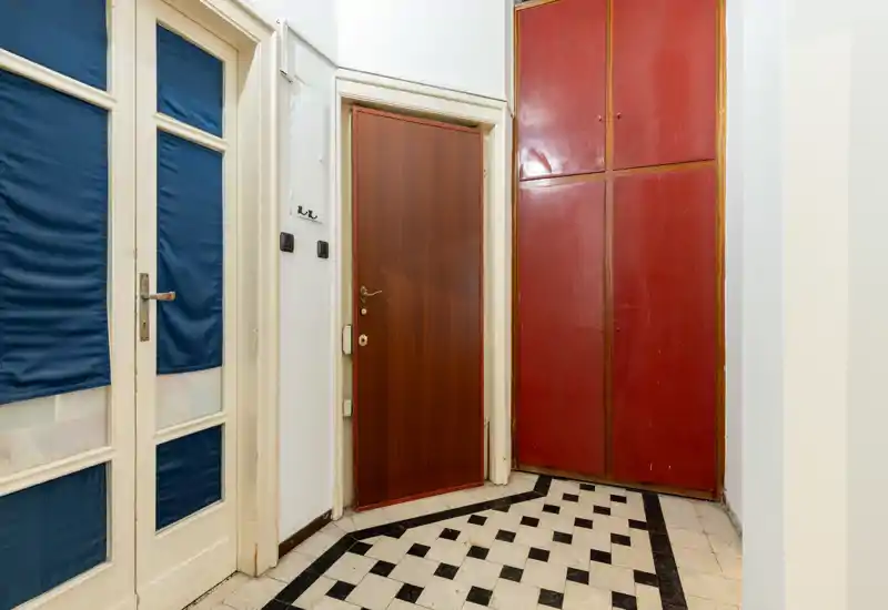 Entrada luminosa y ordenada con suelo de baldosas en blanco y negro, puerta de madera y armario empotrado rojo — un espacio que causa buena impresión para un anuncio de alquiler.
