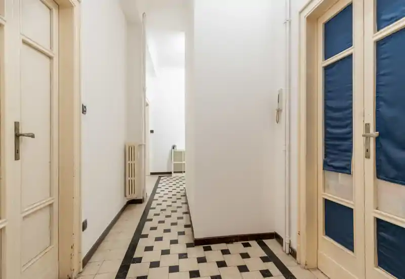 Entrada/pasillo luminoso y estrecho con suelo de baldosas estampadas, paredes blancas y varias puertas hacia estancias adyacentes.