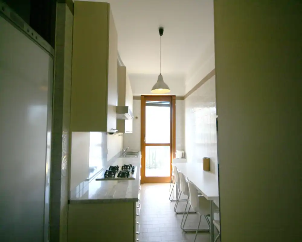 Cocina tipo galería estrecha con encimera efecto mármol, placa de gas empotrada y mesa de desayuno junto a una puerta-balcon luminosa.