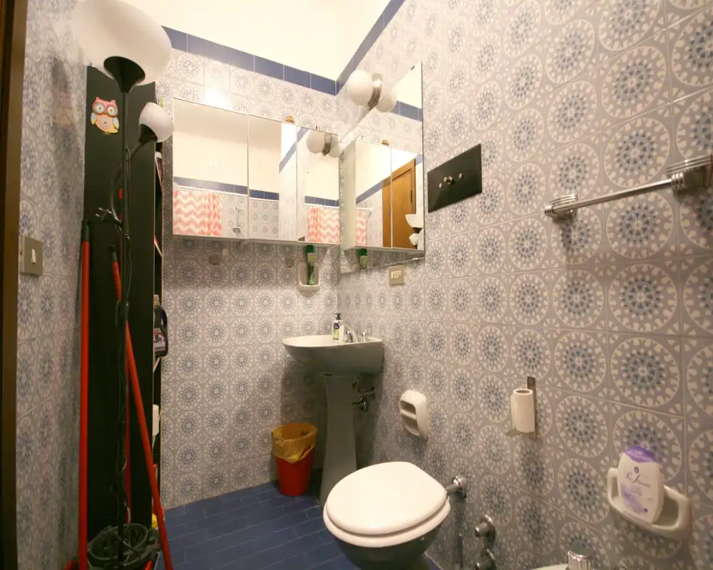 Baño compacto con azulejos de pared estampados, lavabo de pedestal, armario con espejo y inodoro; suelo azul y grifería ordenada.