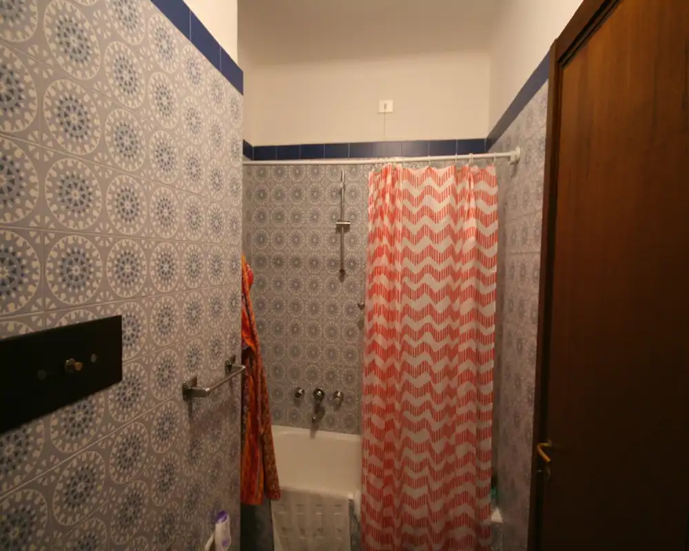 Baño compacto con bañera-ducha, azulejos decorativos azules y cortina de ducha a rayas.