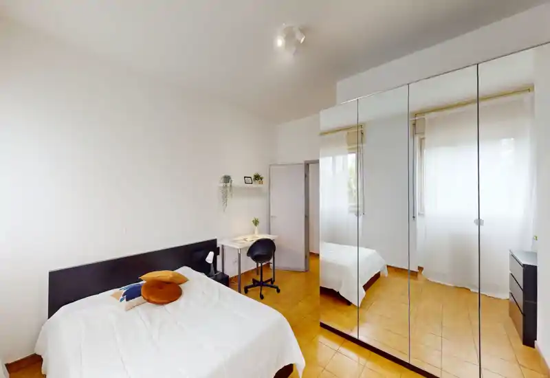 Camera da letto luminosa e moderna con letto matrimoniale, armadio a specchio e una piccola scrivania; arredi neutri e luce naturale che rendono l'ambiente arioso.