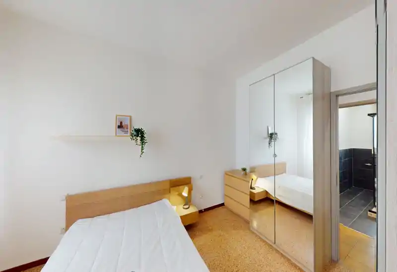 Bright, minimal bedroom with a wooden headboard, bedside lamp and mirrored wardrobe that enlarges the space.
