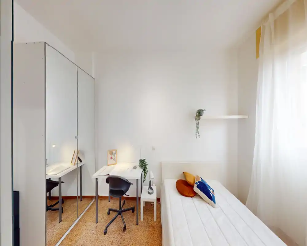 Bright, minimalist bedroom with a single bed, desk and mirrored wardrobe. Natural light and simple decor create a clean, comfortable space ideal for students or solo tenants.