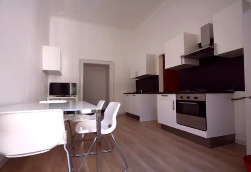 Bright modern kitchen with integrated white cabinets, stainless oven and a glass dining table with white chairs — a minimal, functional space well suited for short stays.