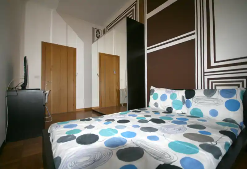 Dormitorio moderno y luminoso con una cama doble grande y ropa de cama estampada, pared de acento geométrica; armario con espejo y pequeña zona con TV/escritorio.