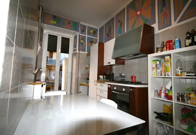 Cocina tipo pasillo bien equipada con cocina de gas, horno, campana extractora y estanterías abiertas; ventana grande que aporta luz natural y una franja decorativa en la parte superior de las paredes.