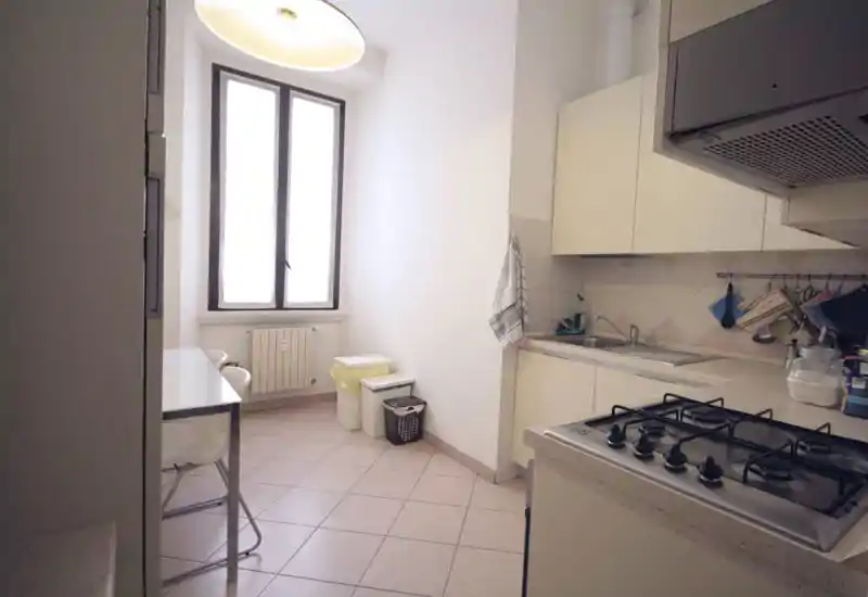 Cucina compatta e luminosa con piano cottura a gas, lavello e pensili; piccolo tavolo vicino alla finestra e pavimento piastrellato rendono lo spazio pratico per colazioni e pasti veloci.