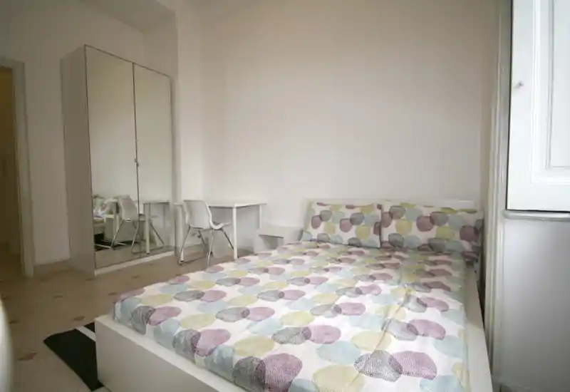 Dormitorio moderno y luminoso con cama doble con edredón estampado, armario con espejo y un pequeño escritorio. La habitación está limpia, amueblada de forma sencilla y recibe buena luz natural.